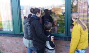 gezin kijkt door raam naar opa in verzorgingstehuis